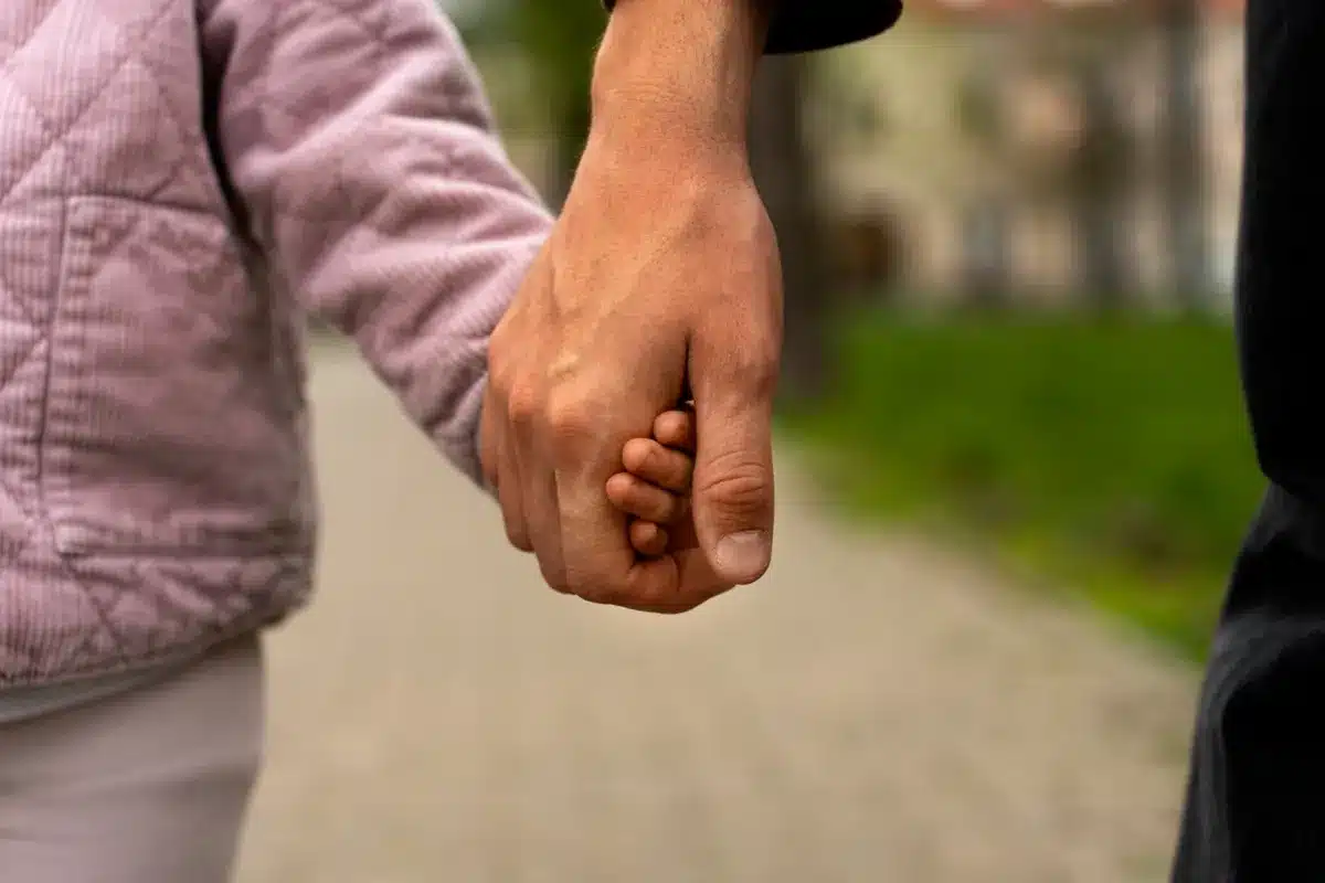 Adoção e salário-maternidade: O que diz a lei? Imagem mostrando um adotante segurando a mão de uma criança, representando o vínculo afetivo e a legislação sobre salário-maternidade para adotantes.