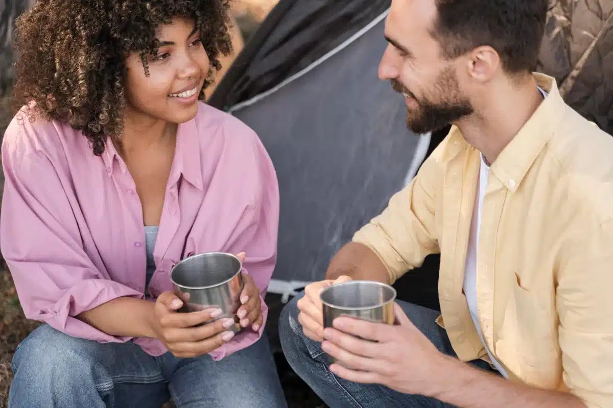 Dinâmica da troca nas conversas Casal sorrindo e trocando olhares durante uma conversa ao ar livre, com copos nas mãos