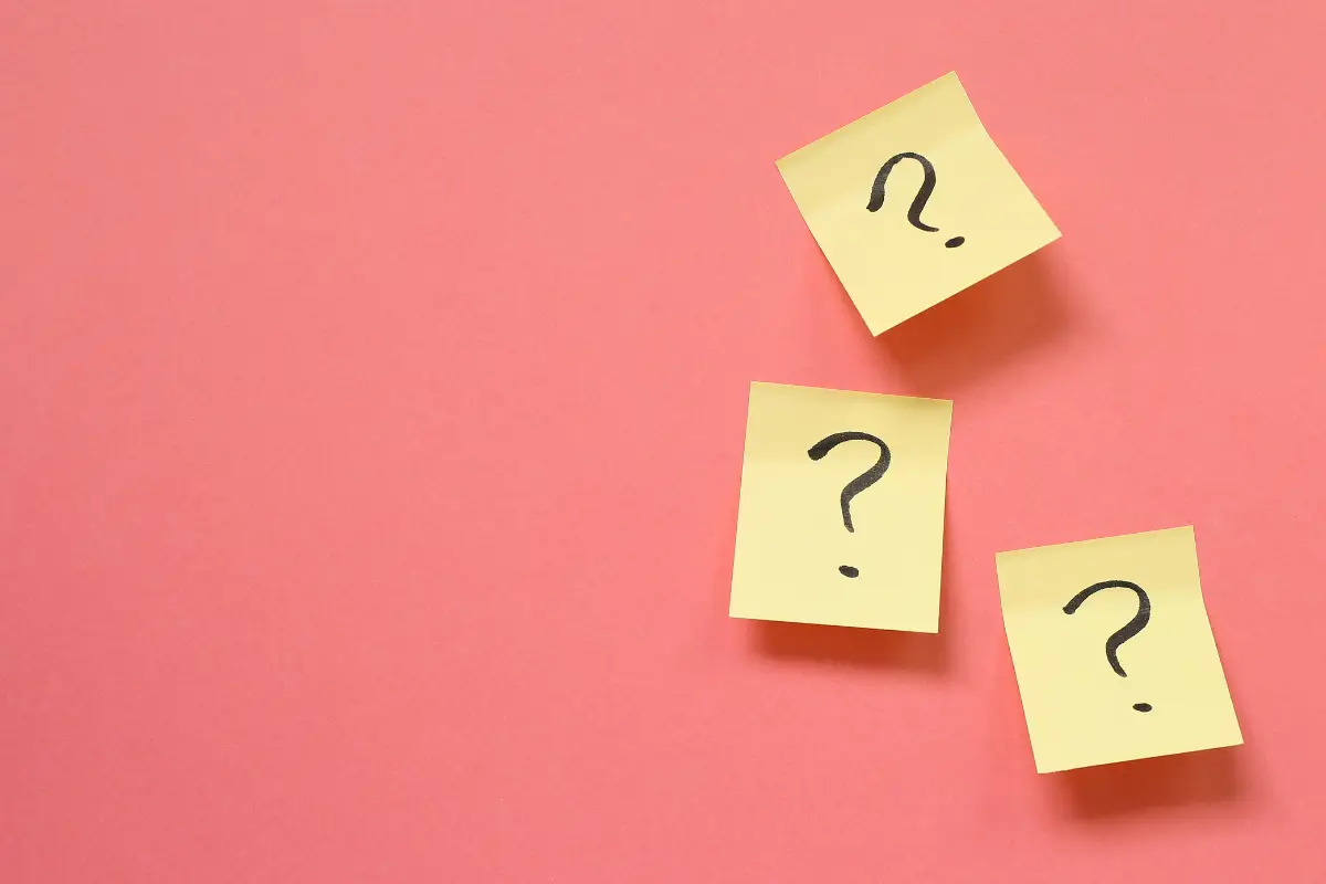 Post-its amarelos com pontos de interrogação desenhados, em fundo rosa, representando dúvidas.