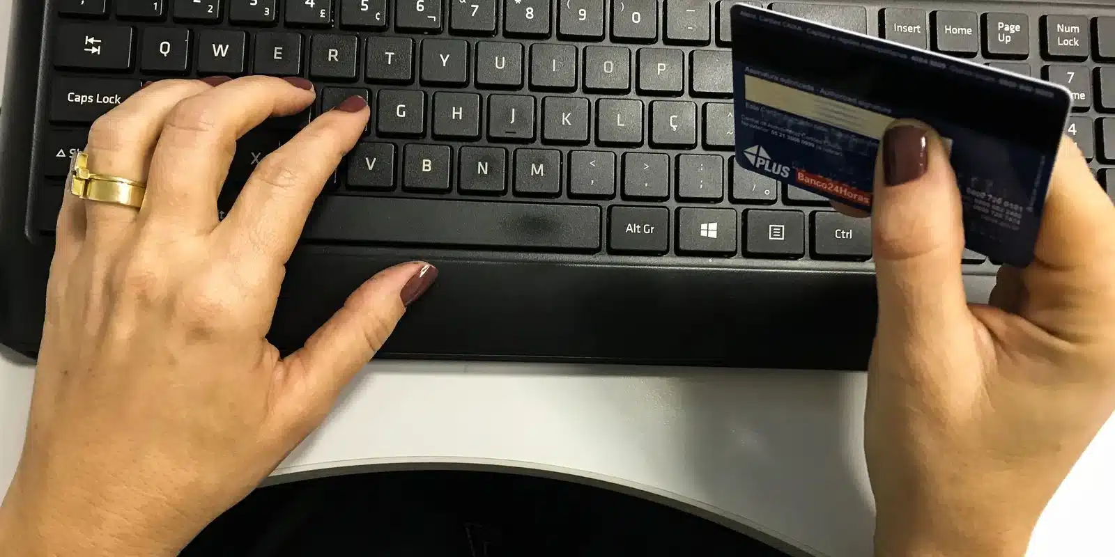 Mão segurando um cartão de crédito enquanto digita no teclado de um computador.