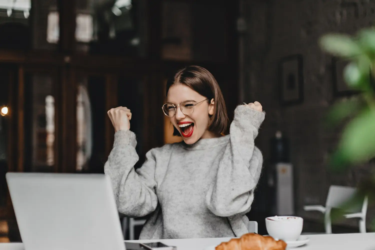 Mulher comemorando após superar um desafio Mulher sorrindo e comemorando enquanto trabalha no computador, representando a conquista ao enfrentar desafios.