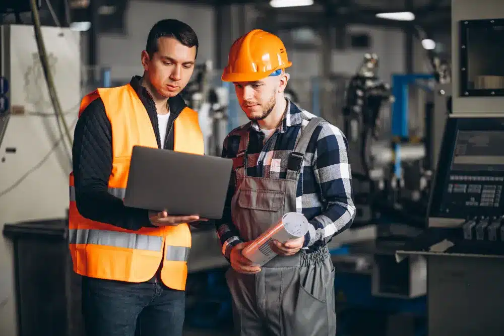 Engenheiros Mecânicos em Ação no Setor Industrial Dois engenheiros em ambiente industrial discutindo projetos e inovações, simbolizando a importância dos engenheiros mecânicos.