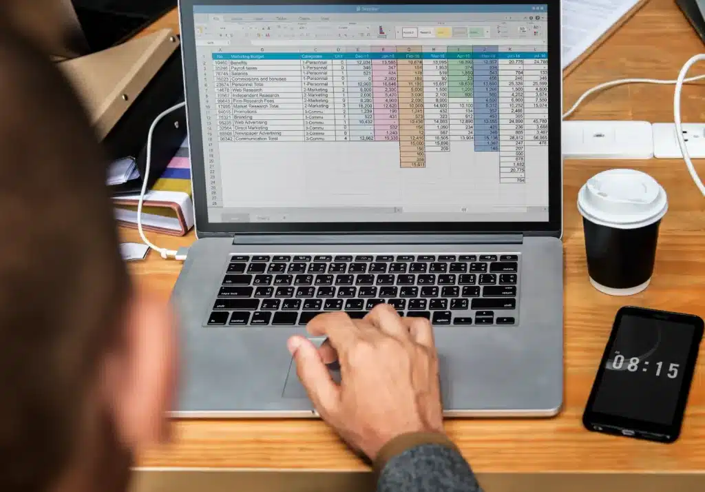 Curso de Excel do Pensar Cursos: Aprenda a usar Excel para sua carreira Pessoa utilizando um laptop para trabalhar em uma planilha de Excel, mostrando um cálculo orçamentário