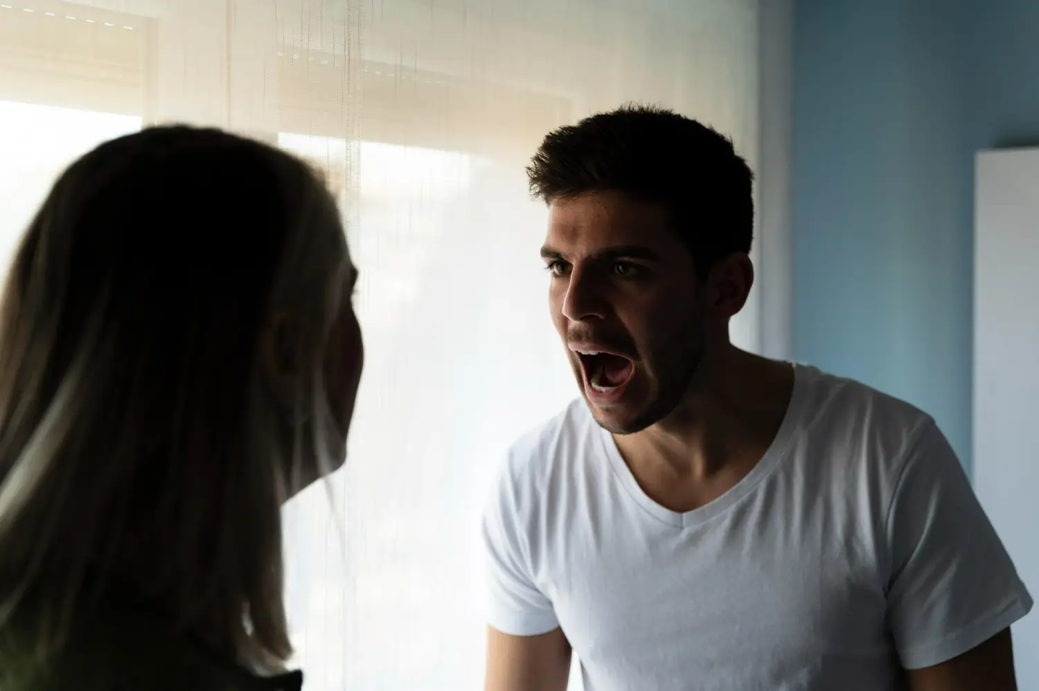 Conflito e desvalorização emocional Homem gritando enquanto mulher olha com expressão frustrada, representando uma situação de desvalorização emocional.