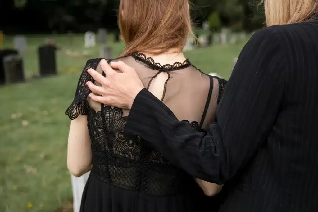 Consolo durante o luto no cemitério Mulher sendo consolada durante o luto, com um gesto de apoio ao fundo do cemitério.