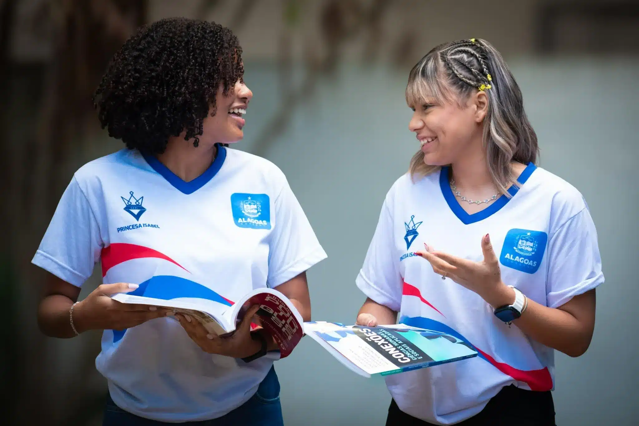 Estudantes beneficiados pelo Bolsa Escola 10 em Alagoas Estudantes felizes conversando e segurando materiais escolares, representando o benefício do Bolsa Escola 10 em Alagoas.