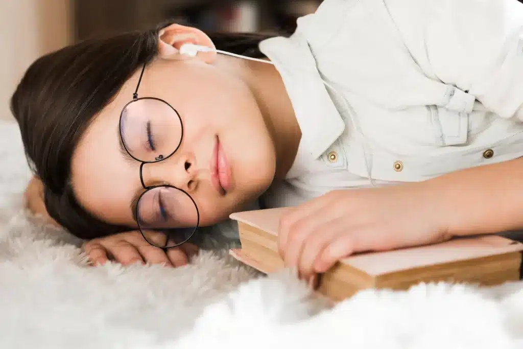 Como a lembrança dos sonhos pode influenciar a saúde mental? Jovem dormindo com um livro nas mãos, representando a conexão entre sonhos e saúde mental