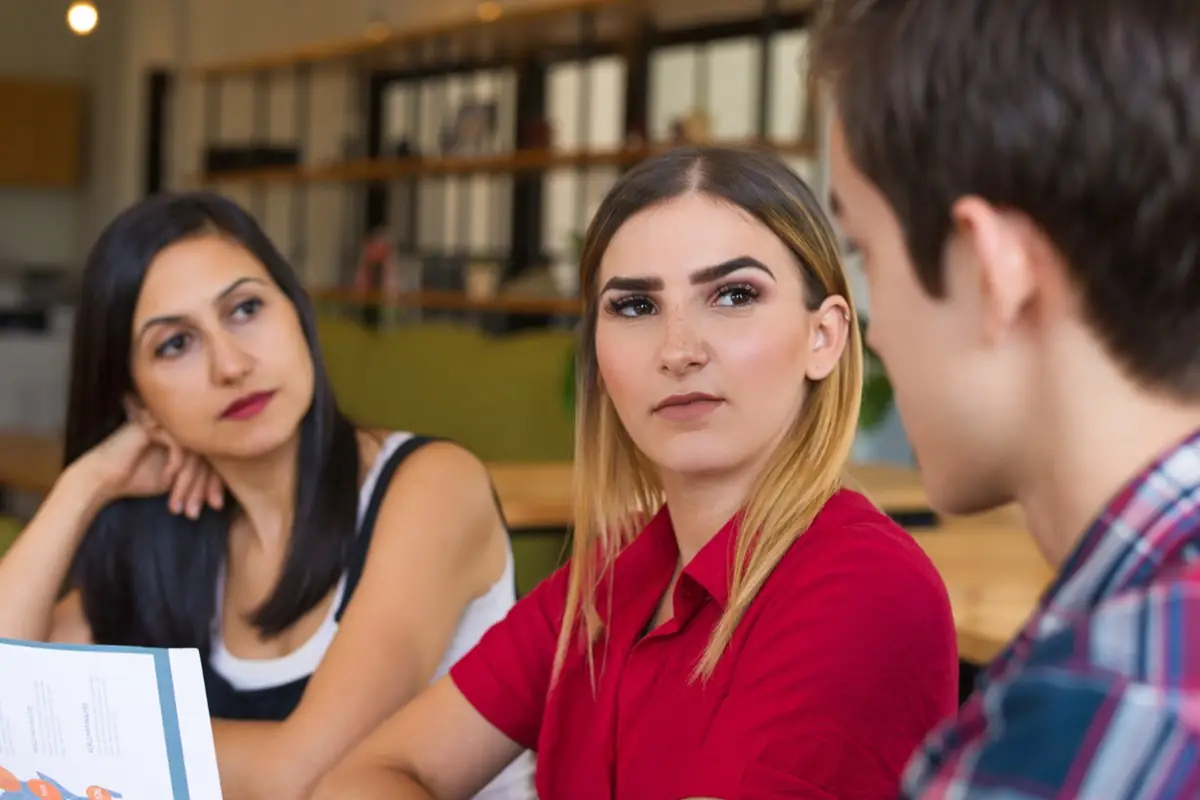 Desconfiança em ambientes sociais: como identificar sinais de falsidade Mulheres observando com desconfiança enquanto ouvem um homem falar.