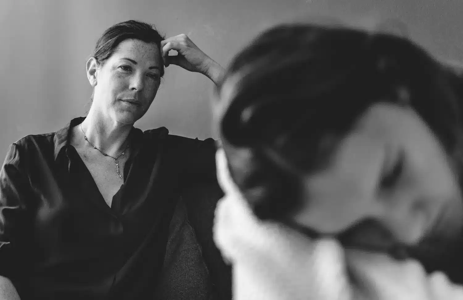 Mulher olhando com expressão fria enquanto outra pessoa aparece cabisbaixa em primeiro plano, simbolizando manipulação emocional.