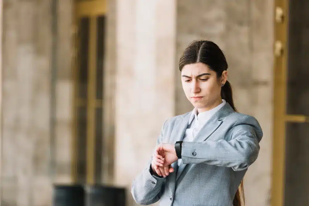 Estratégias para se tornar mais pontual e organizado. Mulher olhando para o relógio com expressão séria, representando a preocupação com pontualidade.