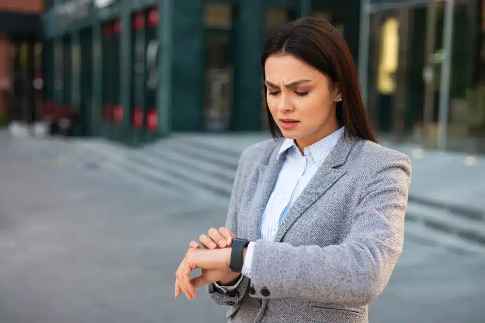 Mulher de terno olhando preocupada para o relógio, simbolizando ansiedade com o horário.