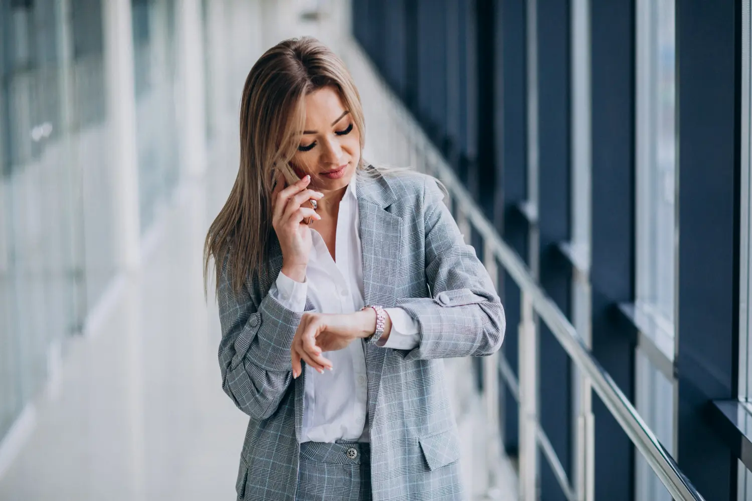 Pontualidade no ambiente profissional Mulher de terno olhando as horas no relógio enquanto fala ao celular em ambiente corporativo.