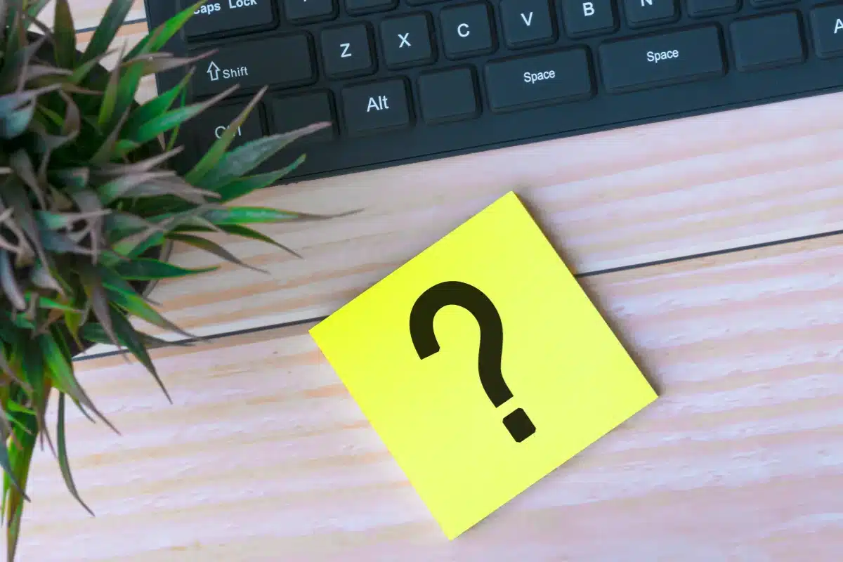 Post-it amarelo com um ponto de interrogação preto sobre fundo de madeira e teclado.