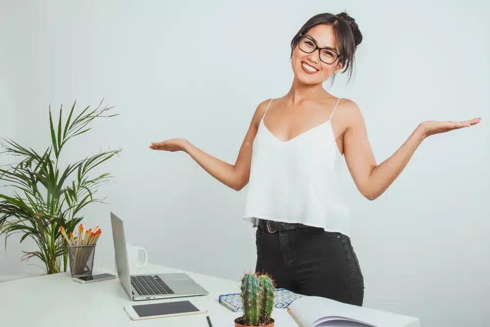 Mulher sorridente em um ambiente de trabalho com um laptop e um cacto sobre a mesa.