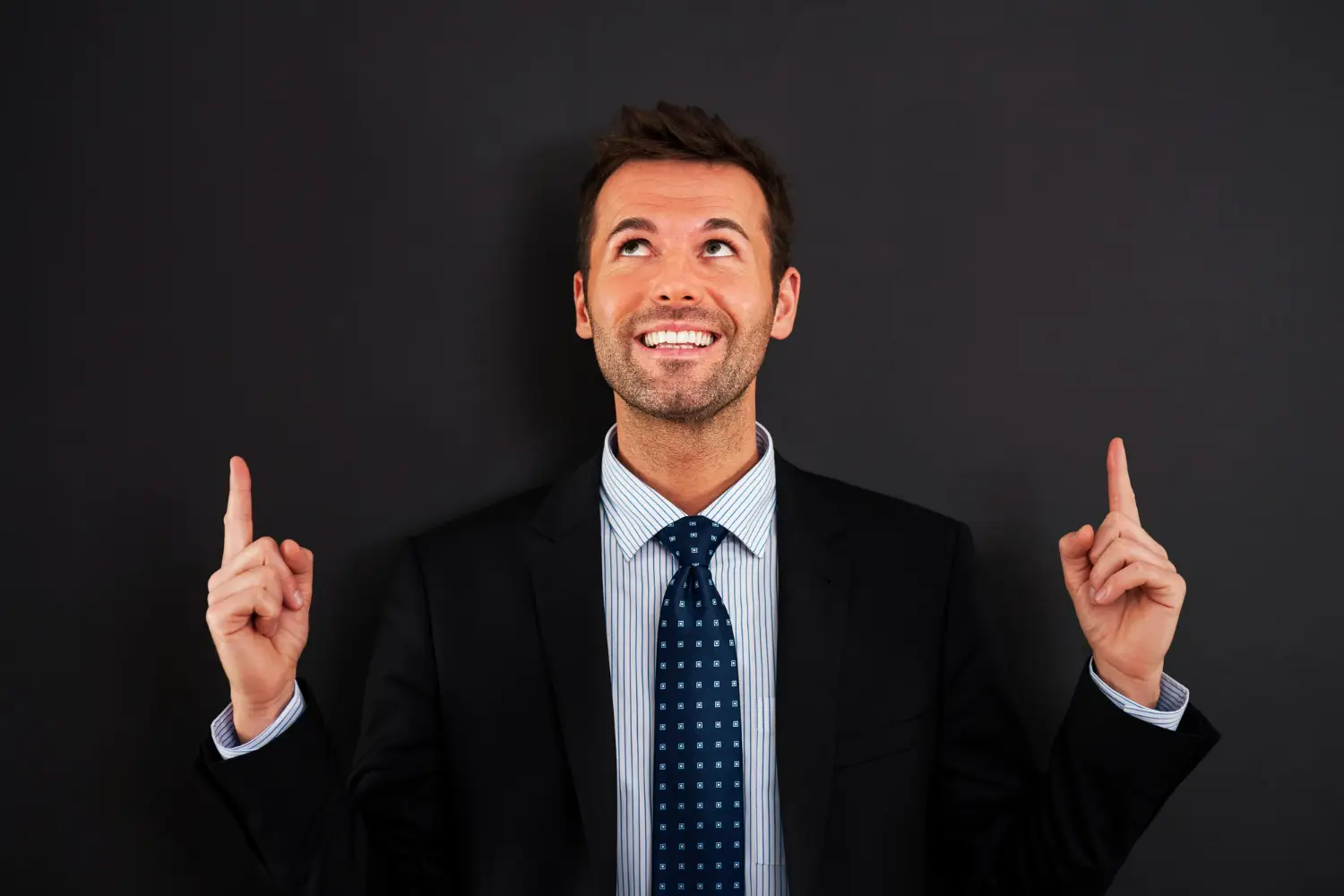 Homem de terno sorrindo e apontando para cima, demonstrando confiança e otimismo.