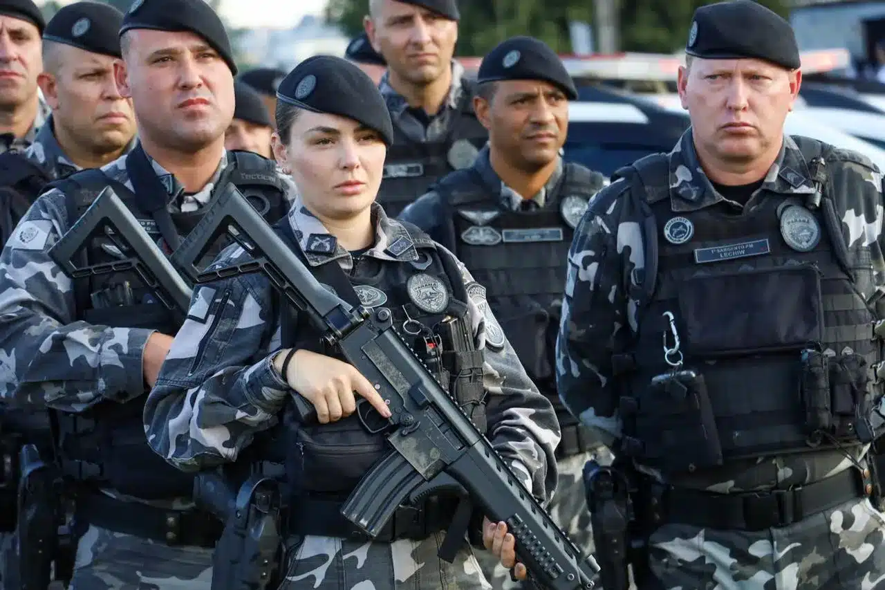 oliciais militares com fardamento camuflado e armamento, preparados para ação.