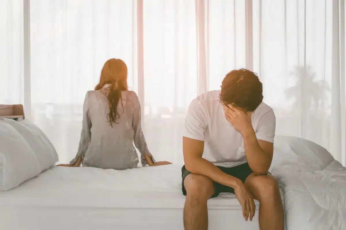 Desgaste emocional Casal afastado na cama, com um clima de tristeza e distanciamento, representando conflitos emocionais em um relacionamento.
