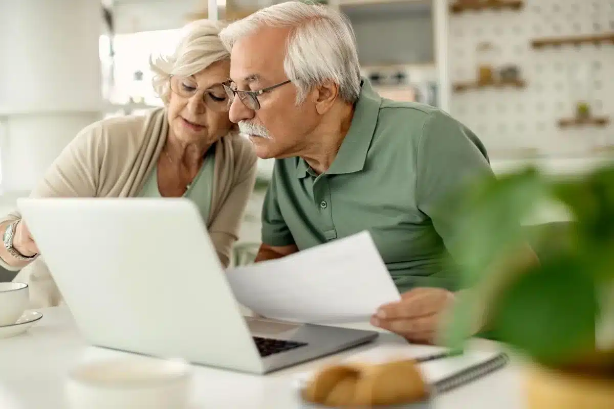 veja como o reajuste do salário mínimo afeta os beneficiários do INSS casal de idosos analisa documentos no notebook em casa