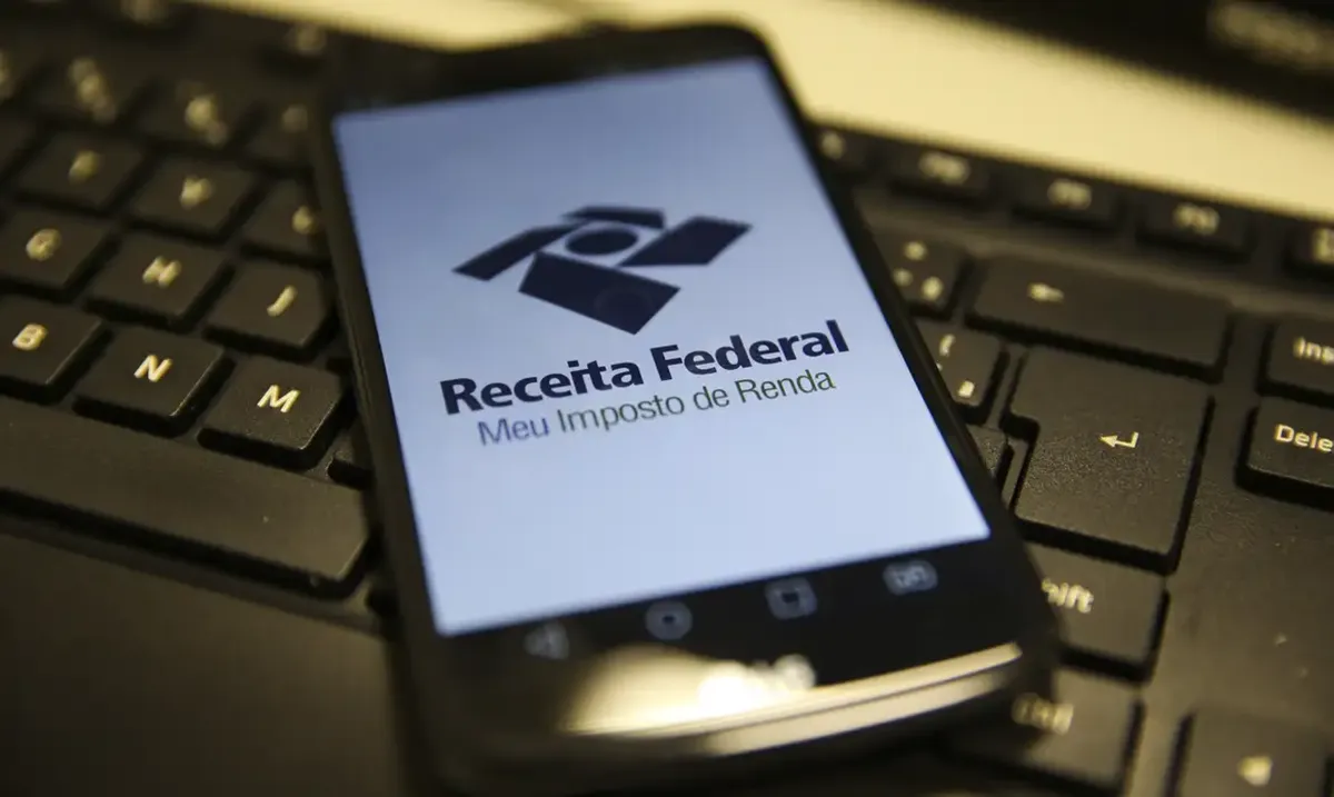 Como declarar o saque-aniversário no IR de 2025 Celular sobre teclado de computador com o aplicativo da Receita Federal aberto.