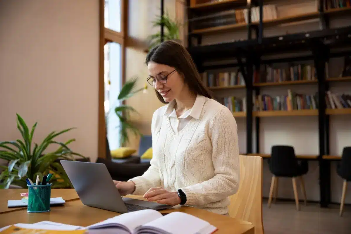 Inteligência Artificial e Machine Learning: Cursos de curta duração mais lucrativos para os próximos 10 anos Mulher sorridente utilizando o laptop para explorar cursos de qualificação profissional.