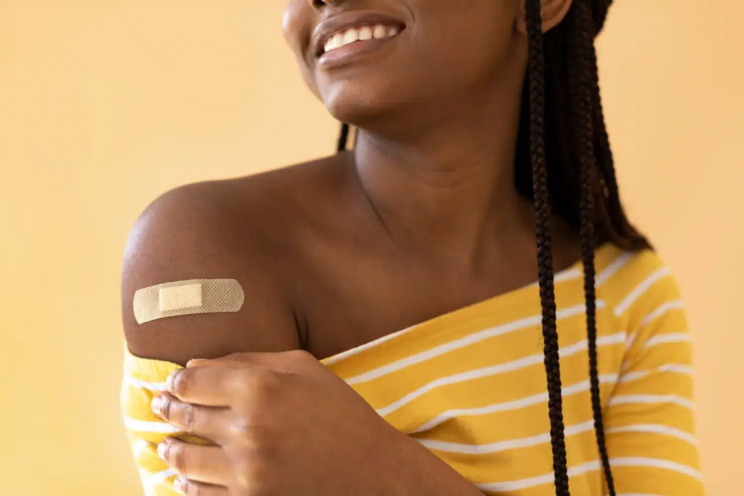 Aplicação de band-aid no ombro, mostrando como o cuidado é simples e eficaz. Mulher sorrindo e com band-aid no ombro.