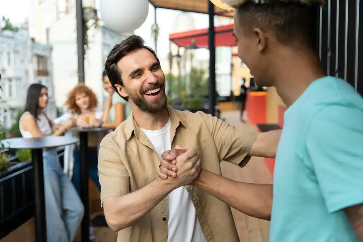 Busca por validação social pode esconder baixa autoestima Homem sorrindo ao cumprimentar outra pessoa, representando busca por aceitação