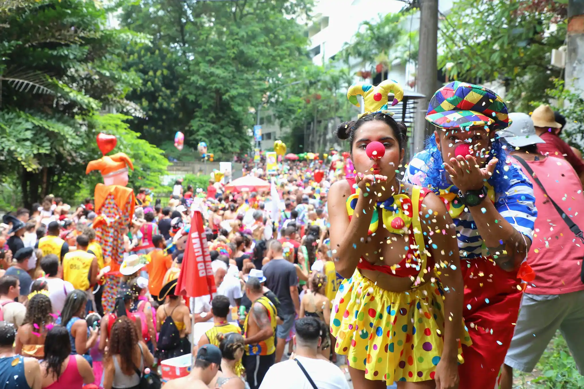 Foliões se divertindo no Carnaval com fantasias coloridas de palhaços e muita alegria nas ruas. Quando é o próximo Carnaval?