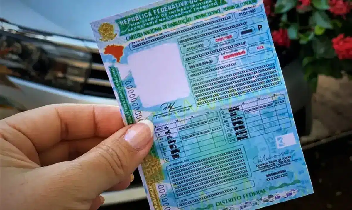Carteira de motorista nas mãos: acesso gratuito pela CNH Social Pessoa segurando carteira nacional de habilitação próxima a um veículo