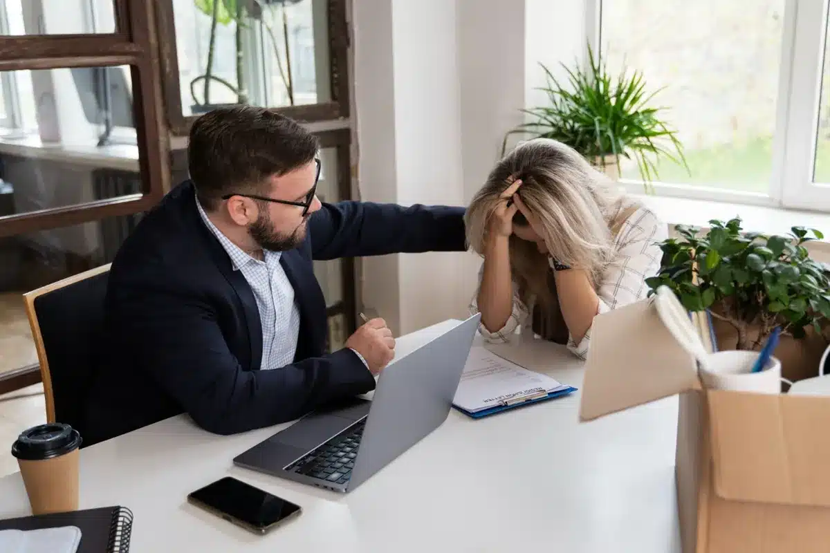homem conforta colega de trabalho visivelmente abalada em ambiente corporativo