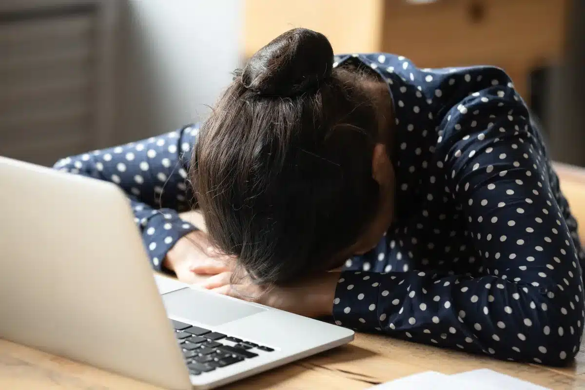 Cansaço e frustração no trabalho Mulher com a cabeça abaixada sobre o teclado do computador, mostrando sinais de cansaço e frustração no ambiente de trabalho.