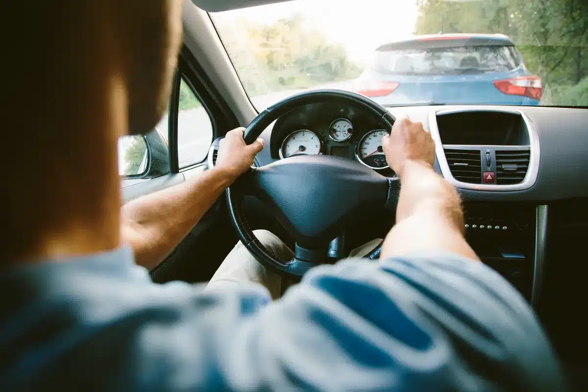 Homem dirigindo enquanto observa o painel do carro, em tráfego lento.