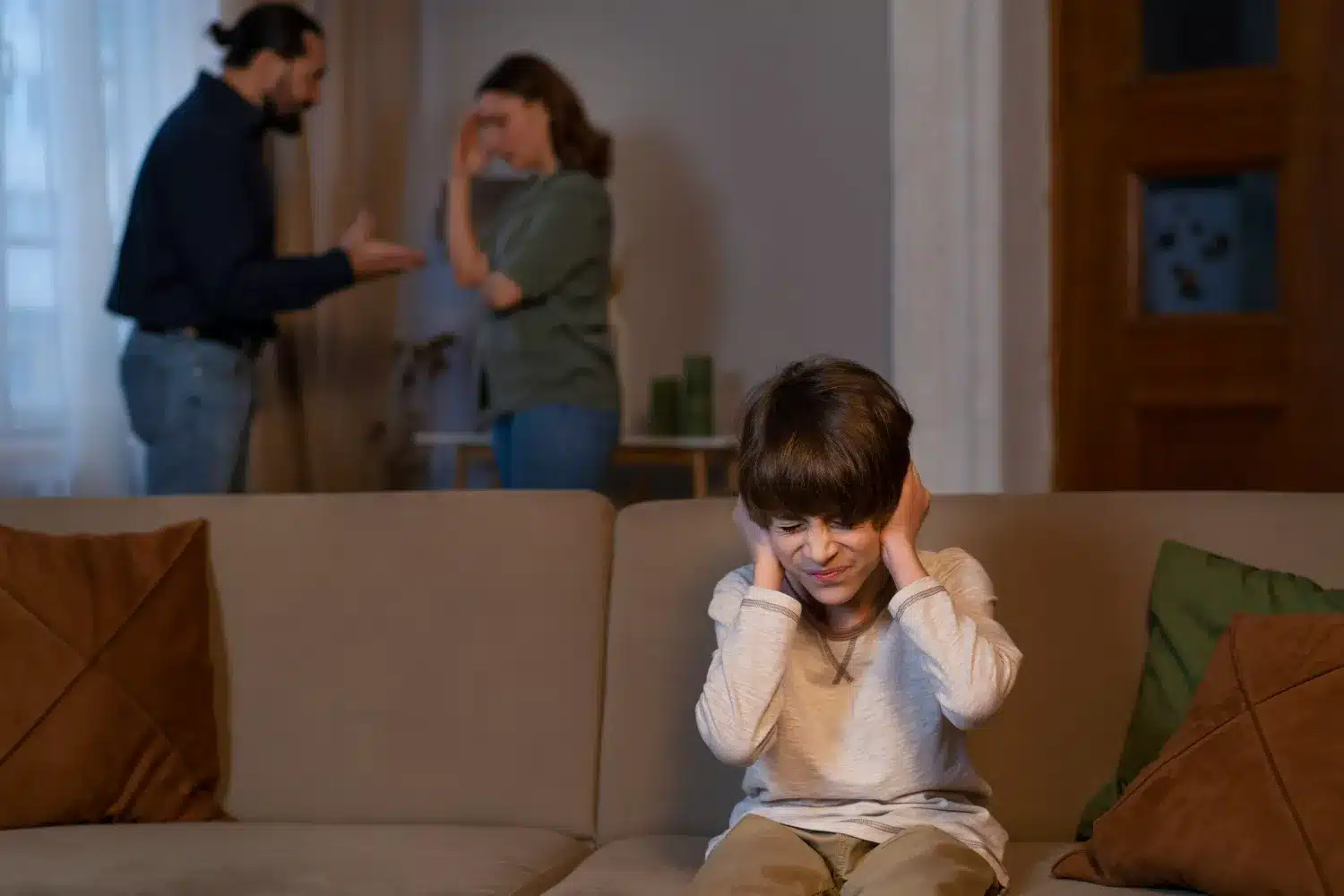 Criança tapando os ouvidos enquanto pais discutem ao fundo, representando o impacto emocional de conflitos familiares.