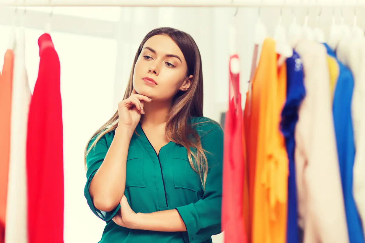 Mulher refletindo sobre qual roupa escolher em meio a opções coloridas