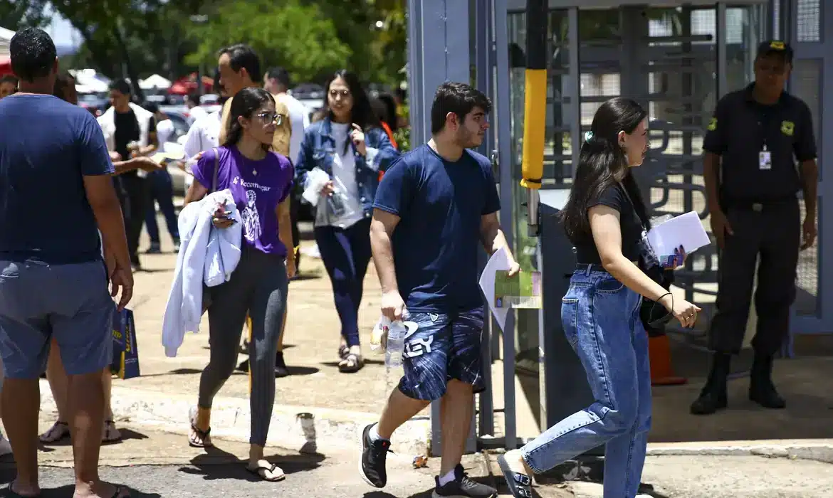 Prova de processo seletivo Grupo de pessoas chegando para realizar atividades em evento, com foco em jovens se dirigindo à entrada do local.