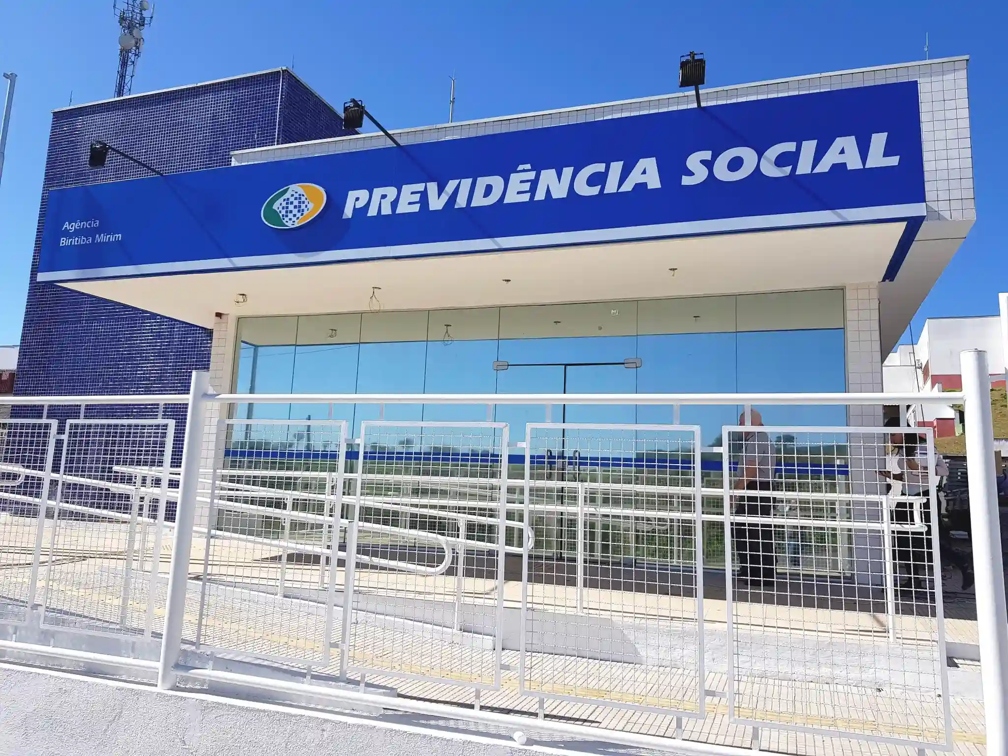 Agência da Previdência Social Fachada de agência da Previdência Social com portas de vidro e rampa de acesso.