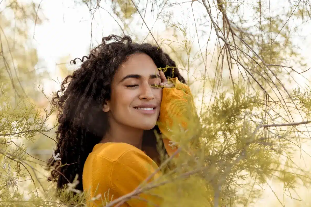 mulher sorridente de olhos fechados aproveita momento de tranquilidade na natureza