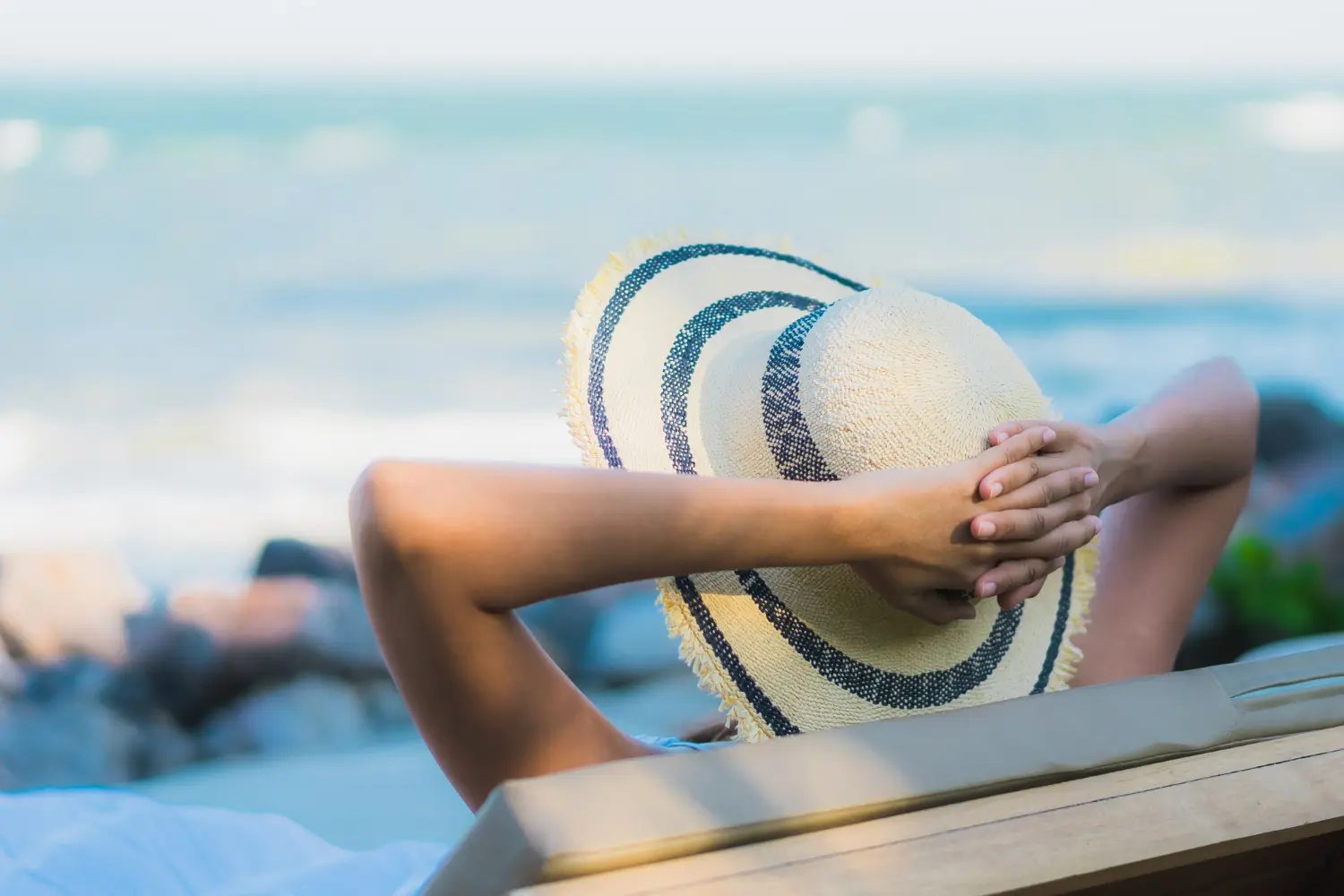 Pessoa relaxando na praia com chapéu, aproveitando o feriado e o descanso à beira-mar.