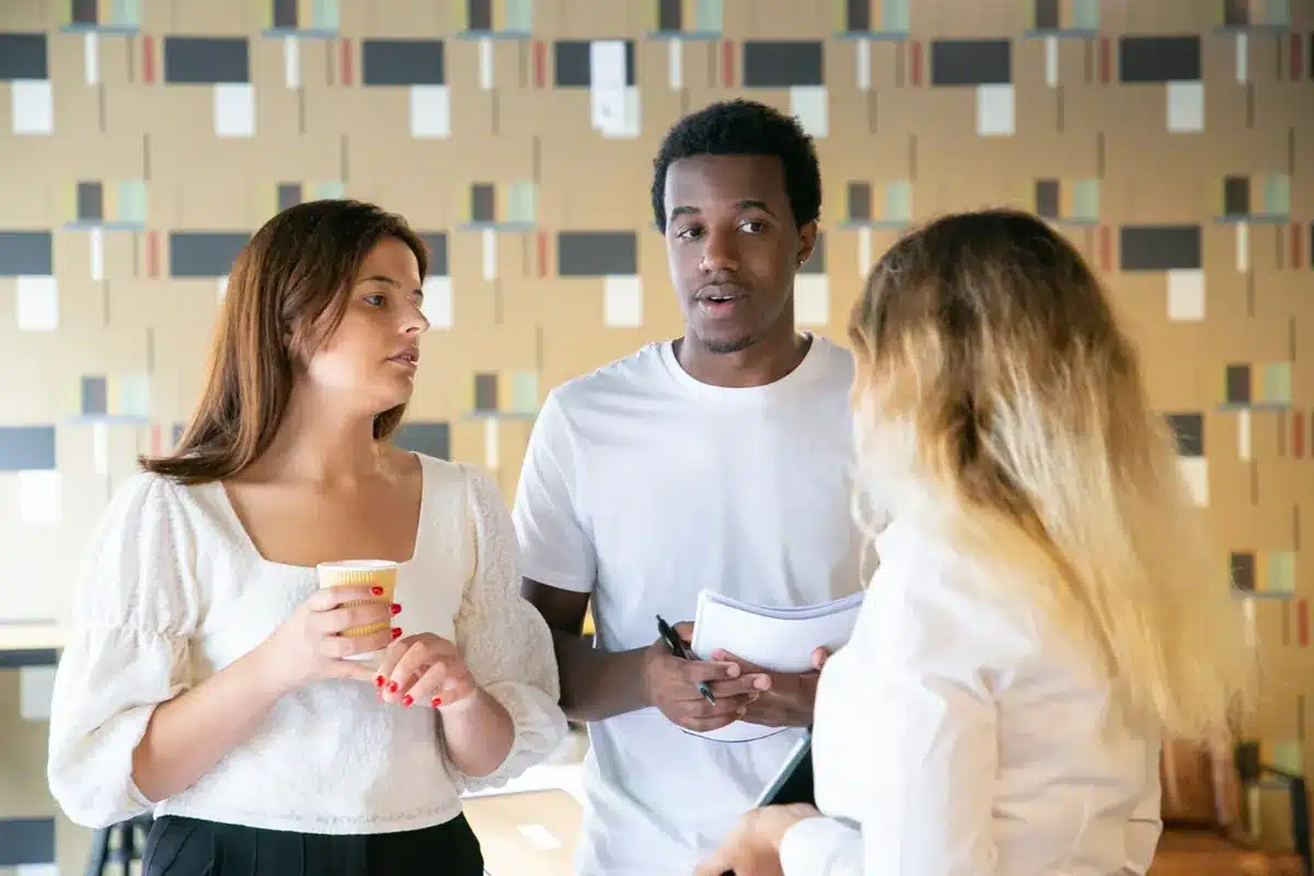 A frase que pode transformar uma discussão Três pessoas conversam em grupo, com um homem falando e duas mulheres ouvindo atentamente.
