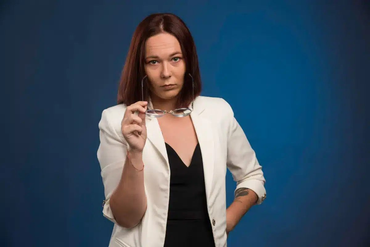 Mulher com expressão séria e olhar de reprovação, segurando óculos, representando a ideia de como algumas frases podem ser interpretadas como arrogantes.