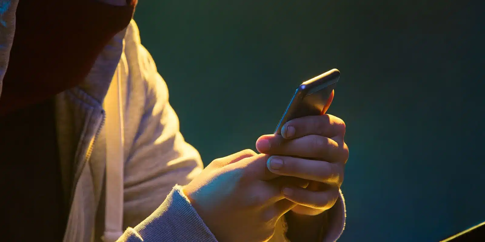 Protegendo o celular com a função de bloqueio e Pessoa de Confiança. Pessoa com capô usando celular, representando a segurança de bloqueio no celular.