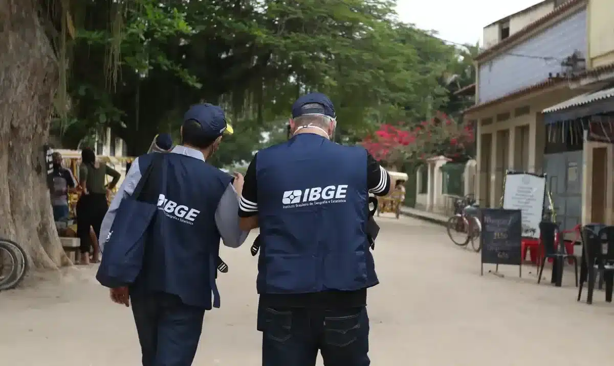 Pesquisadores do IBGE caminhando por uma rua, com coletes de identificação, durante a coleta de dados do Censo.
