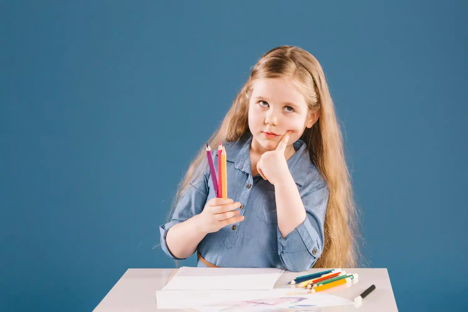 Menina com cabelo longo, segurando lápis coloridos e pensando, refletindo sobre o plural de lápis.