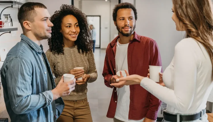 O impacto do volume da voz nas relações interpessoais Grupo de pessoas em conversa amigável, segurando copos, discutindo de forma descontraída e equilibrada, em um ambiente moderno de escritório