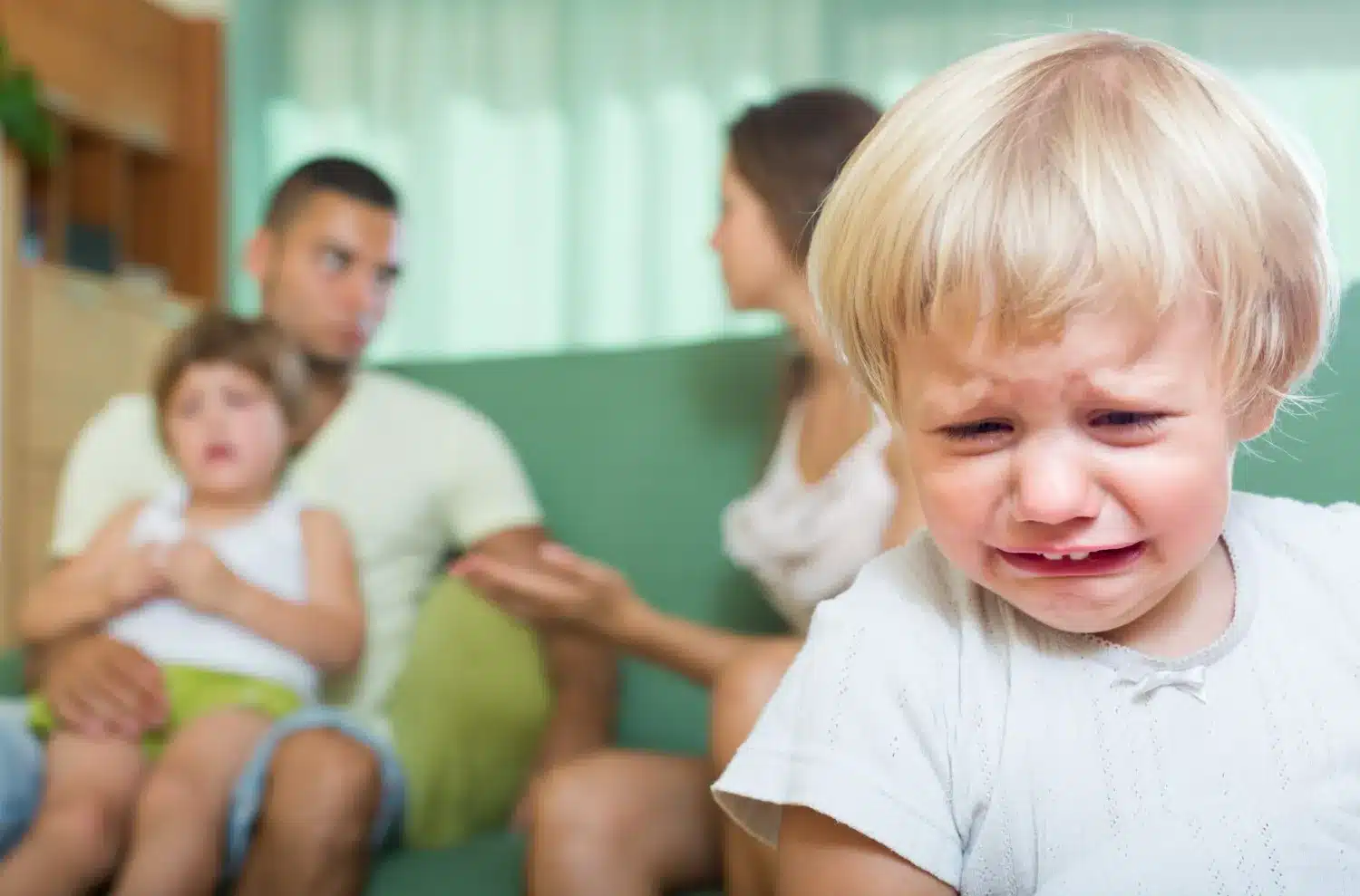 O impacto das discussões familiares na infância. Criança chorando em primeiro plano enquanto os pais discutem ao fundo.