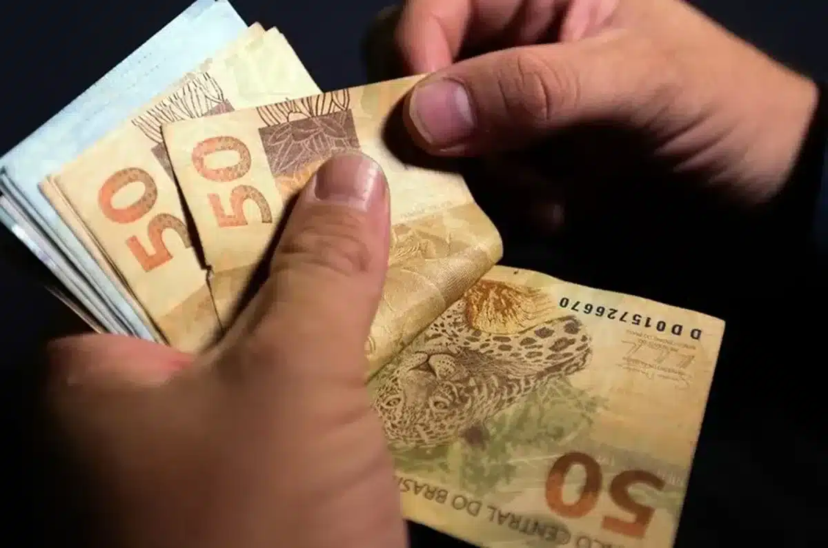 Pessoa segurando notas de R$ 50, simbolizando o pagamento do abono salarial pelo INSS.