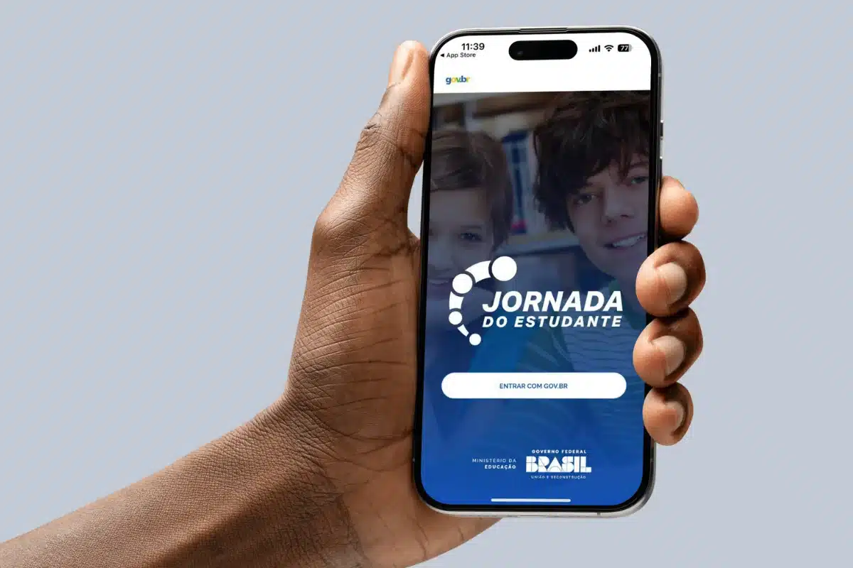 Tela inicial do app Jornada do Estudante Pessoa segurando celular com o app Jornada do Estudante na tela, mostrando a interface de login.