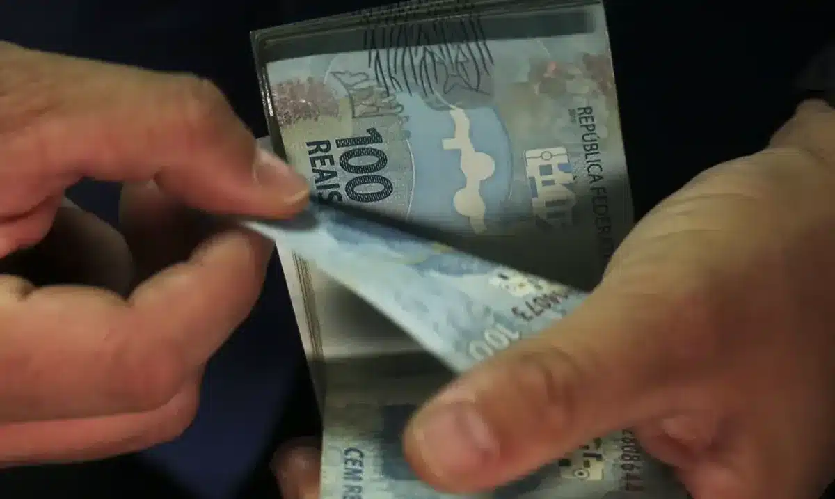 Pessoa retirando notas de 100 reais de uma carteira, representando o valor de depósitos financeiros