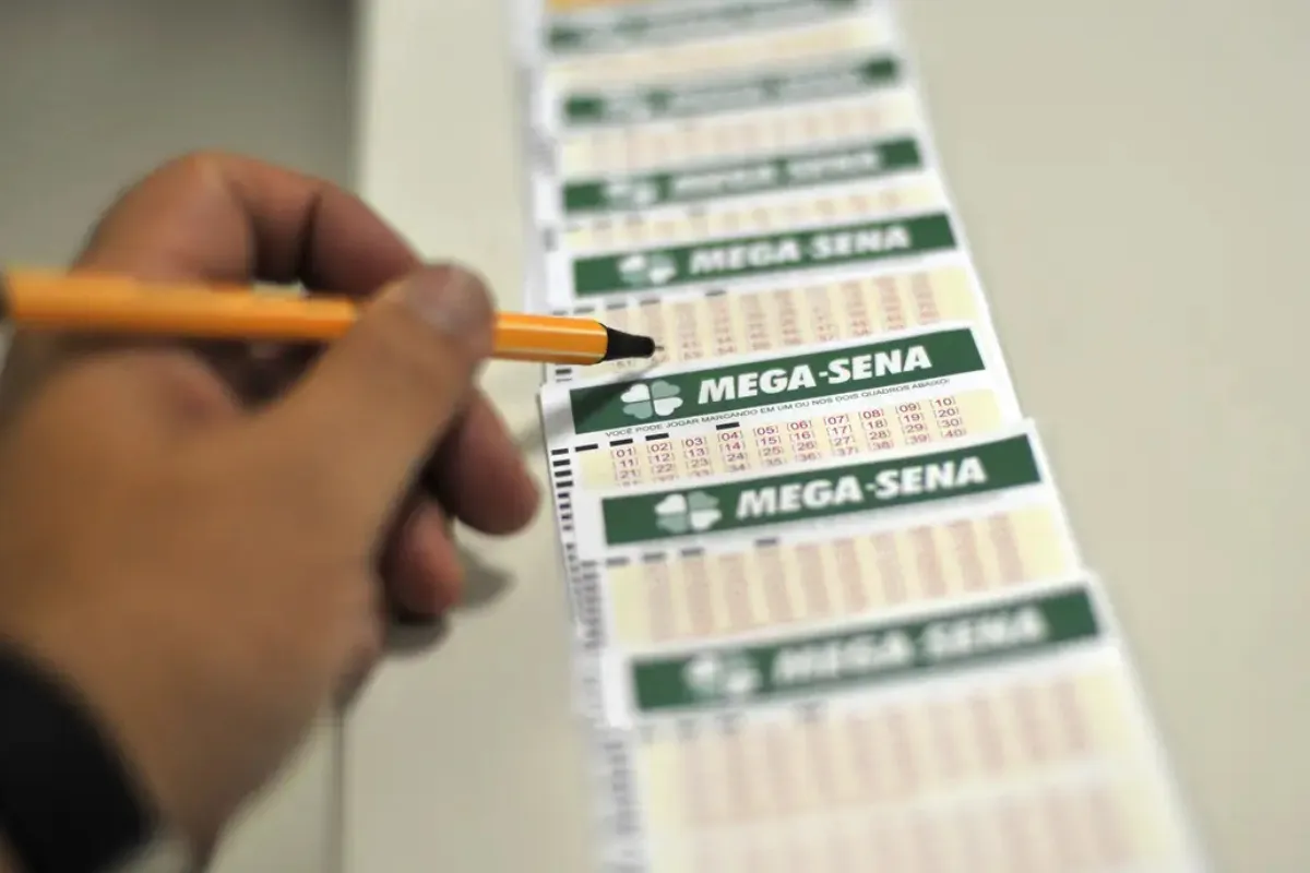 Preenchendo a cartela da Mega-Sena Pessoa usando um lápis para marcar os números na cartela da Mega-Sena.