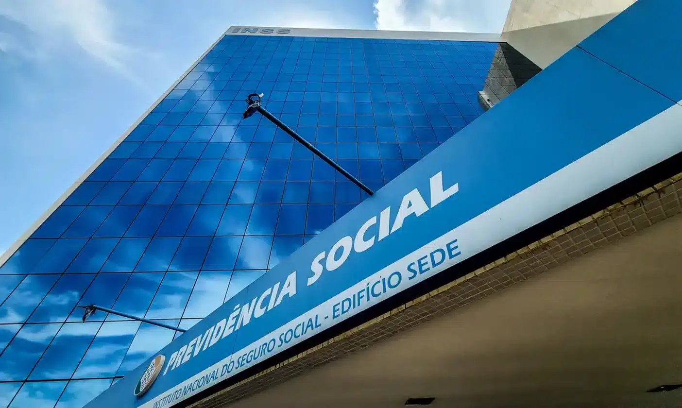 Fachada do prédio do INSS com destaque para a placa 'Previdência Social' e o logo do Instituto Nacional do Seguro Social.