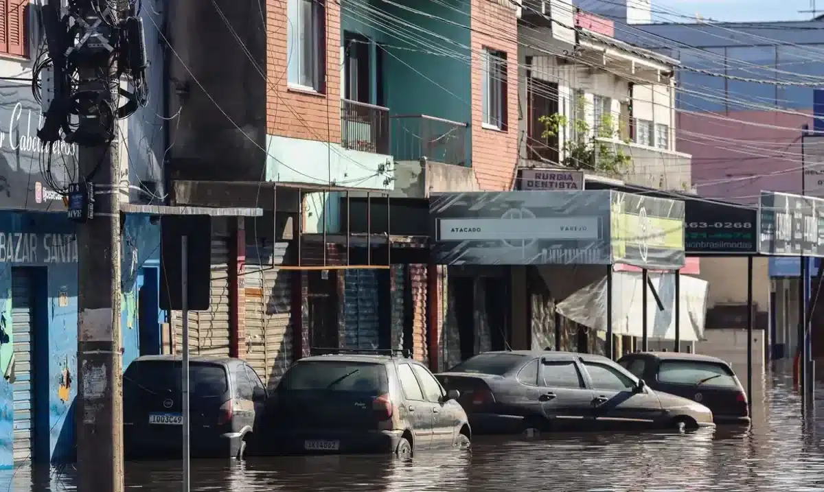 Saque calamidade Rua alagada com carros submersos e fios expostos após enchente.